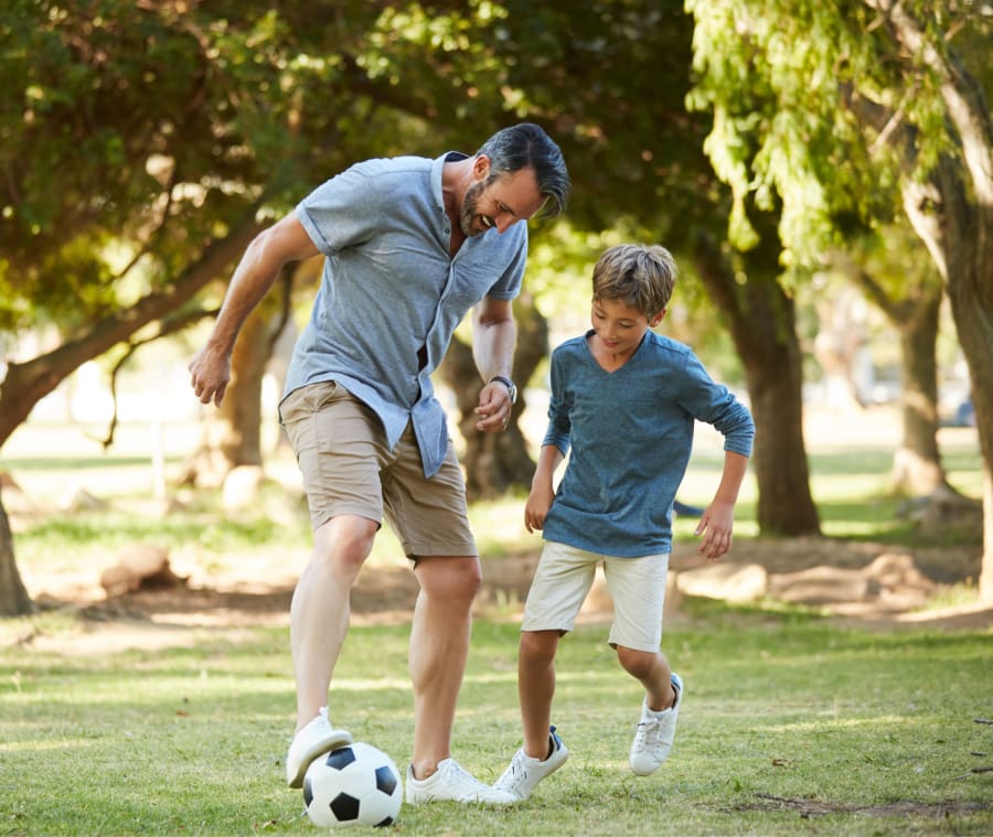 Father and son having fun outdoors, smiling while playing soccer together.