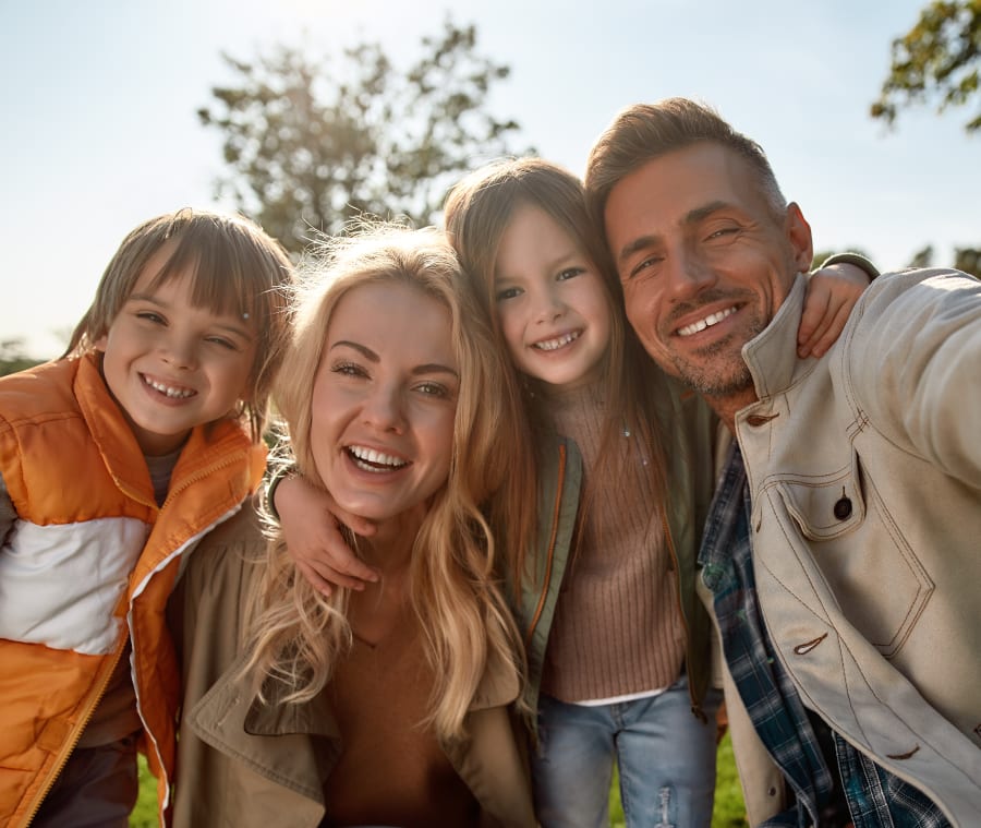 Family of four smiling for a photograph outdoors, enjoying a sunny day together.