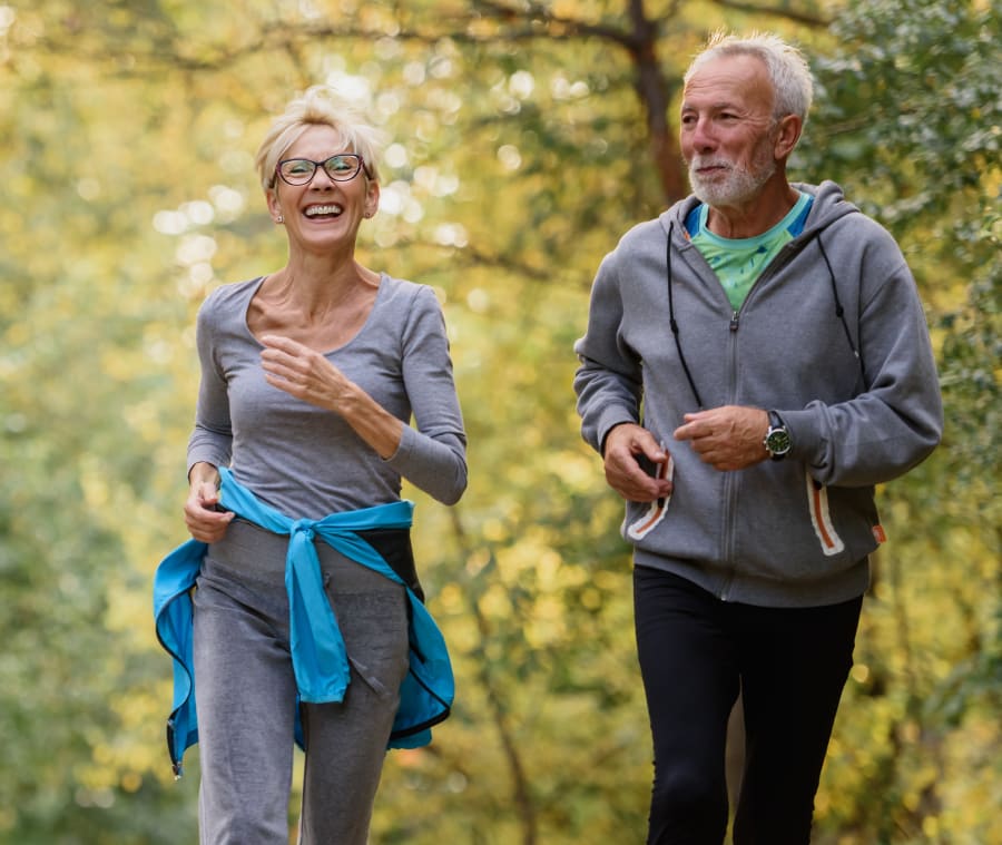 Older woman and man jogging together outdoors, smiling and enjoying their exercise.
