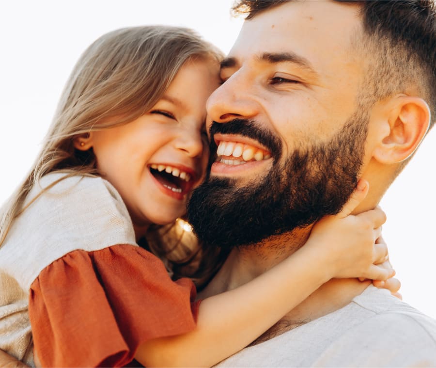 Father and daughter smiling together as she wraps her arms around his neck.