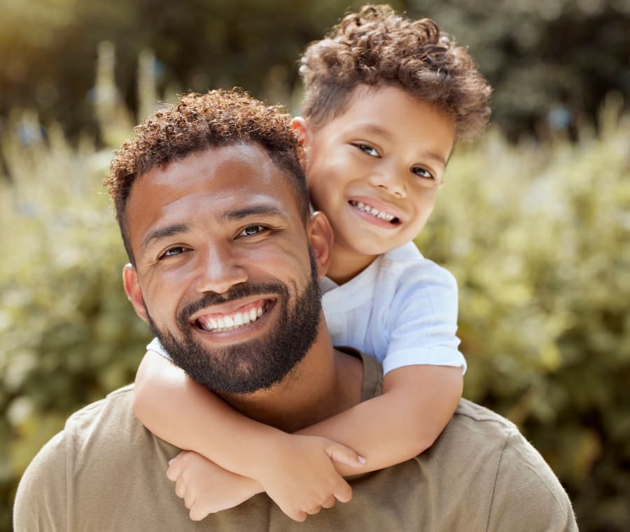 Father and son smiling together as a young boy wraps his arms around his father's neck.