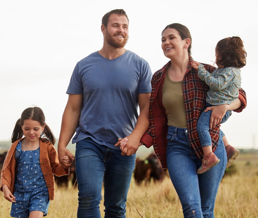 Family of four sitting together on the grass, smiling and blowing bubbles outdoors.
